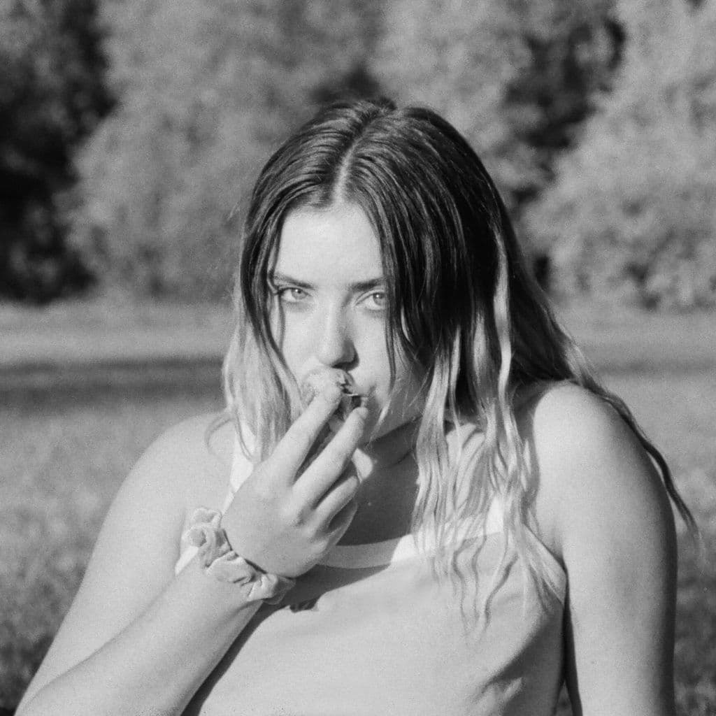 A girl looking into the camera and eating in a park