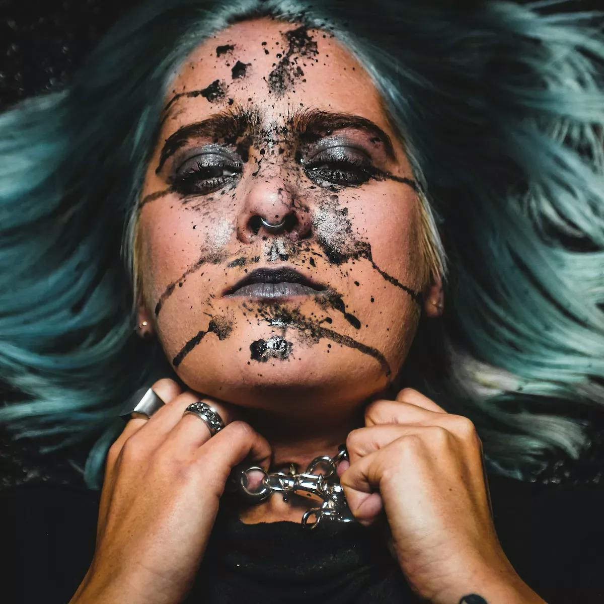 Woman laying down with ink on her face and her hands to her neck