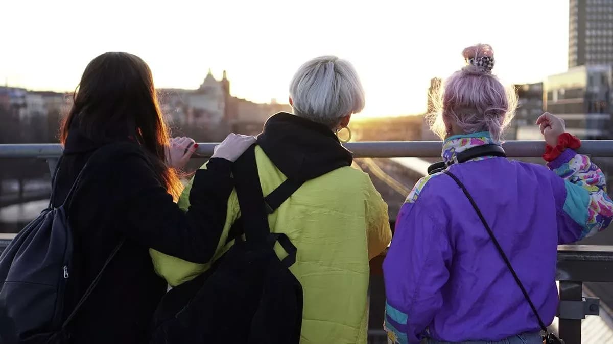 Three people on a bridge facing the sunset