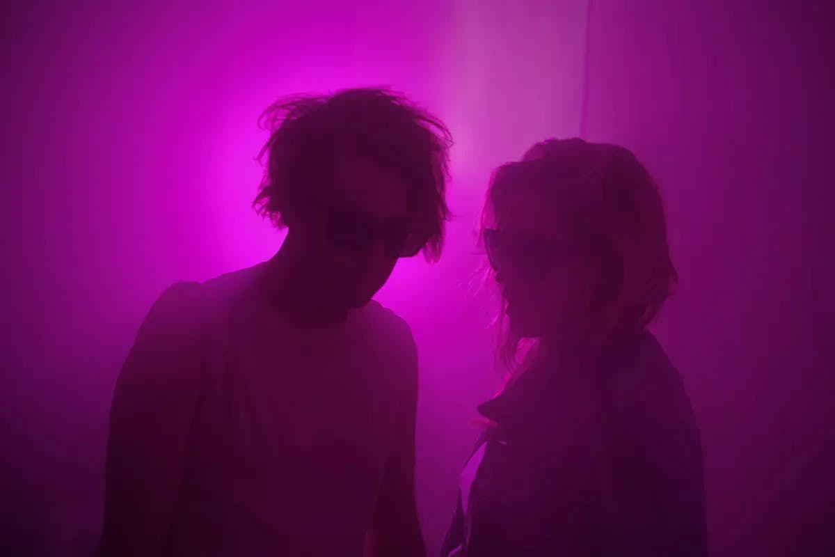 A man and woman standing next to each other wearing shades in purple lighting