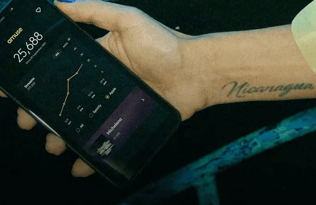 Close-up of a smartphone displaying a music app with statistics. A tattoo reading "Nicaragua" is visible on the person's wrist.