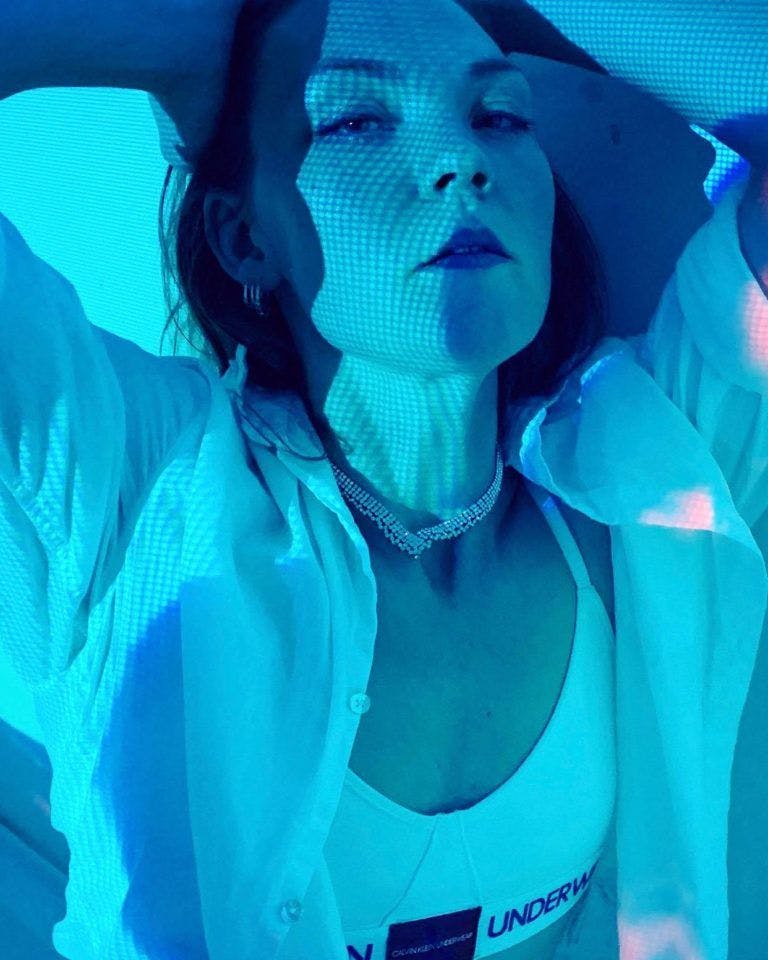 Woman in a blue light with her hands on her head