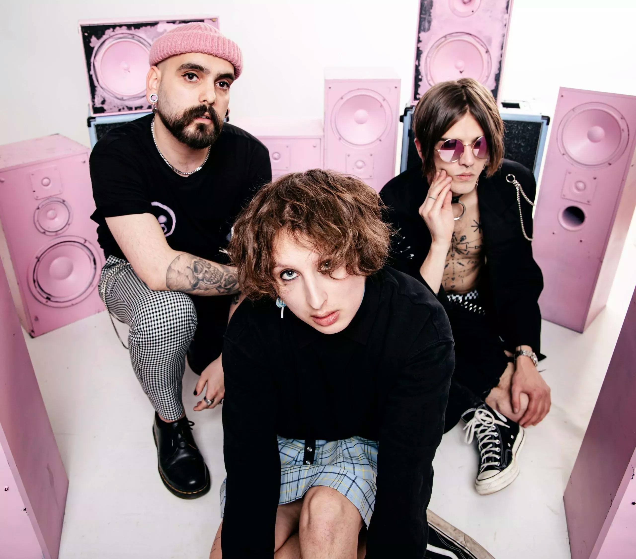 Music group Tribe Friday, lead singer Noah Deutschmann in the middle, guitarist Isak Gunnarsson on the right, and bassist Robin Hanberger-Pérez on the left with pink speakers in the background
